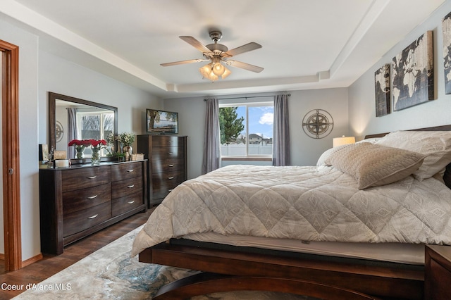 bedroom with a raised ceiling, dark wood finished floors, and a ceiling fan