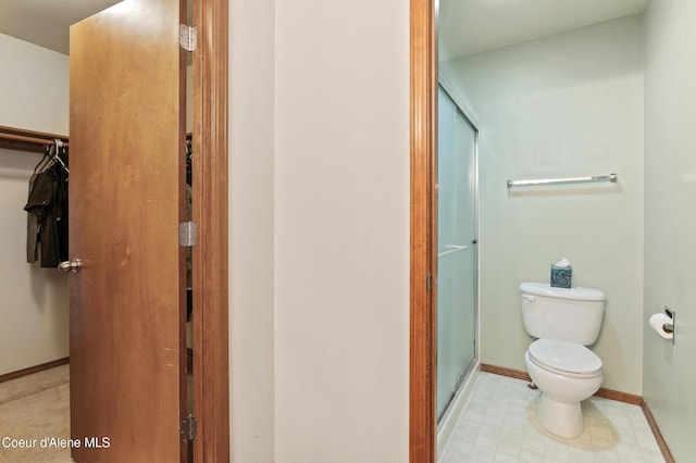 full bathroom with baseboards, a stall shower, a walk in closet, tile patterned floors, and toilet