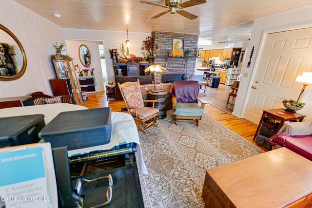 living area featuring a brick fireplace, ceiling fan, and light wood finished floors