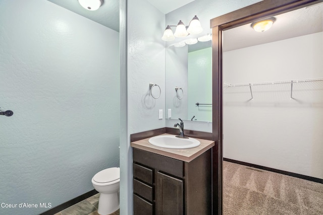 bathroom featuring toilet, vanity, baseboards, a spacious closet, and a textured wall