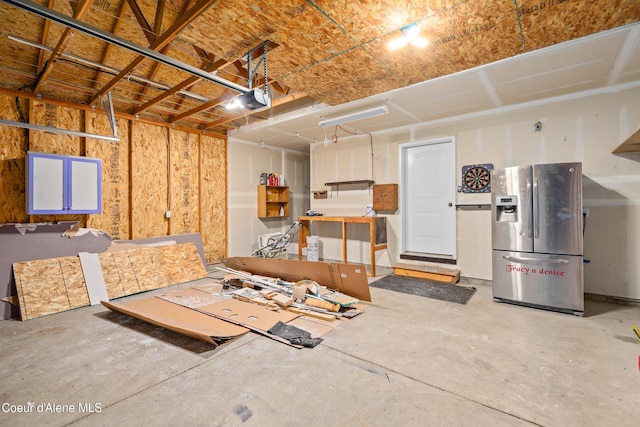 garage with a garage door opener and stainless steel refrigerator with ice dispenser