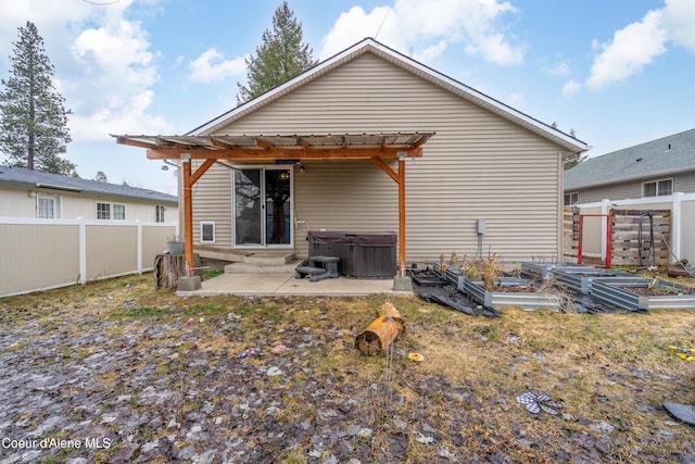 back of house with entry steps, a fenced backyard, a patio area, a vegetable garden, and a hot tub