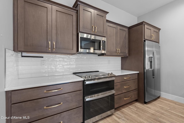 kitchen featuring light wood finished floors, tasteful backsplash, appliances with stainless steel finishes, light countertops, and baseboards