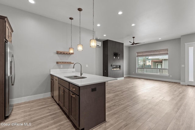 kitchen featuring a sink, a large fireplace, a peninsula, stainless steel fridge with ice dispenser, and dark brown cabinets