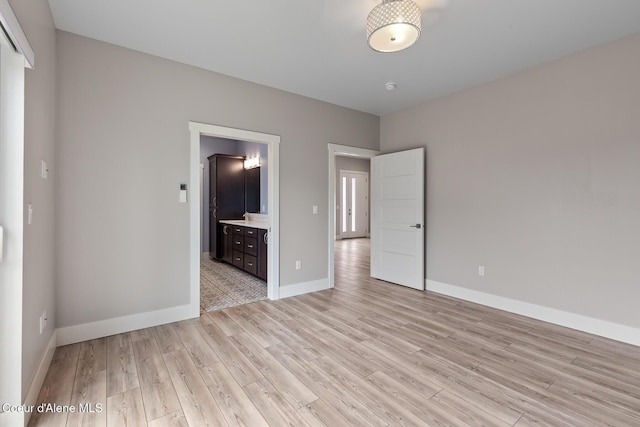 unfurnished bedroom with a sink, baseboards, ensuite bathroom, and light wood finished floors