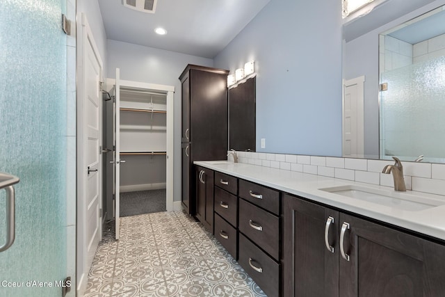 full bathroom with double vanity, a shower with shower door, a walk in closet, and a sink