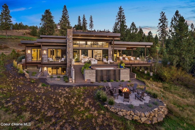 back of property at dusk featuring a wooden deck, stairway, an outdoor fire pit, and a patio