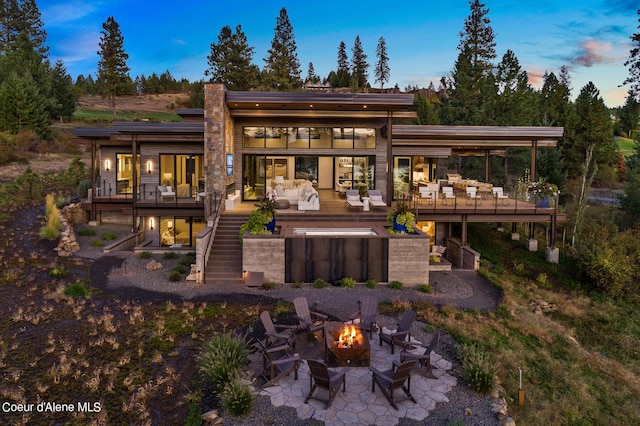 back of property at dusk featuring a patio area, stairway, a wooden deck, and an outdoor living space with a fire pit