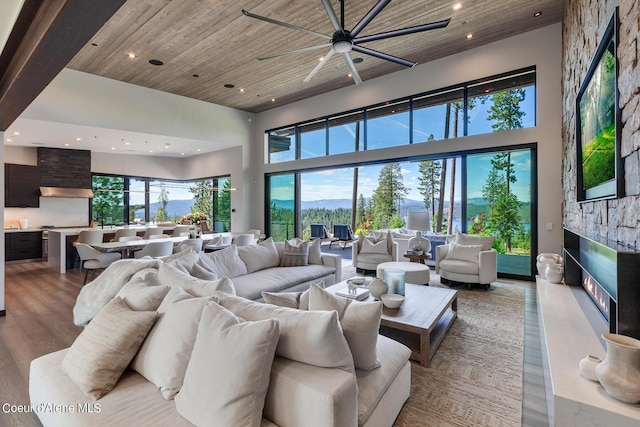 living area featuring light wood finished floors, wood ceiling, recessed lighting, a fireplace, and a high ceiling