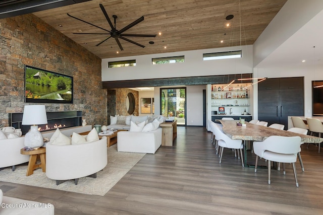 living area featuring wood finished floors, a large fireplace, a bar, wooden ceiling, and a towering ceiling