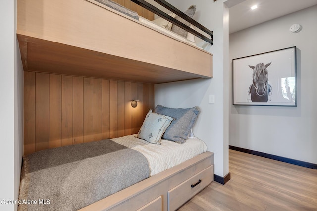 bedroom featuring wood walls, light wood-type flooring, and baseboards