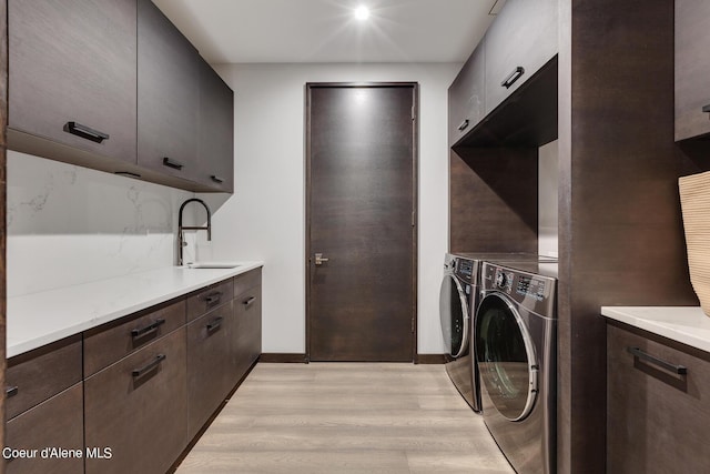 washroom featuring light wood-type flooring, a sink, washer and dryer, cabinet space, and baseboards