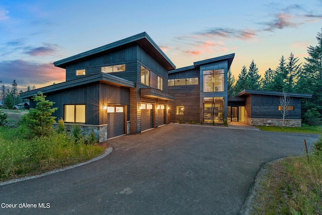 modern home featuring aphalt driveway, stone siding, and an attached garage