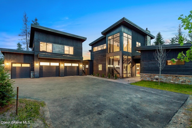 modern home featuring stone siding, driveway, an attached garage, and stairs