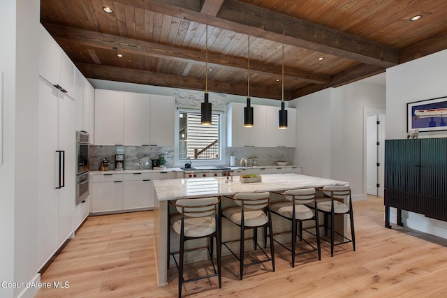 kitchen with a breakfast bar, hanging light fixtures, light wood-style floors, wooden ceiling, and backsplash