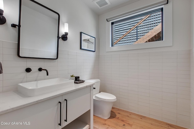 bathroom featuring vanity, wood finished floors, visible vents, tile walls, and toilet