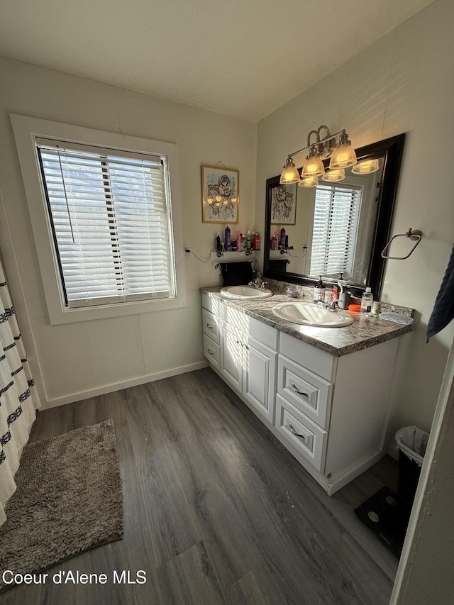 full bath with double vanity, wood finished floors, baseboards, and a sink