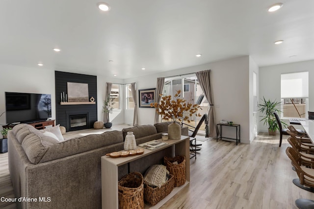 living area featuring recessed lighting, light wood-style flooring, and a large fireplace