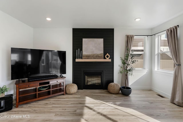 living room featuring visible vents, a large fireplace, baseboards, and wood finished floors