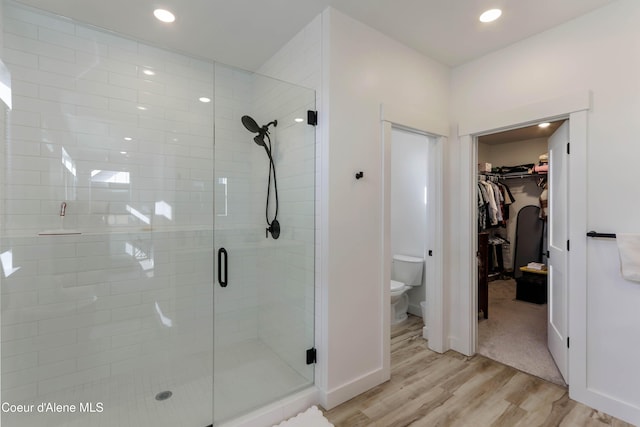 bathroom featuring wood finished floors, recessed lighting, a shower stall, a walk in closet, and toilet