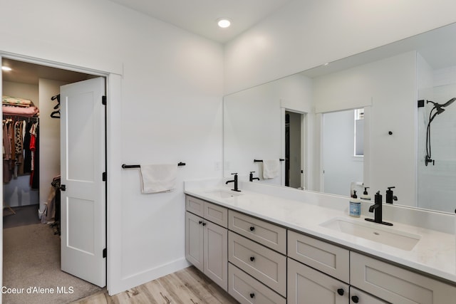 bathroom featuring double vanity, a spacious closet, wood finished floors, and a sink