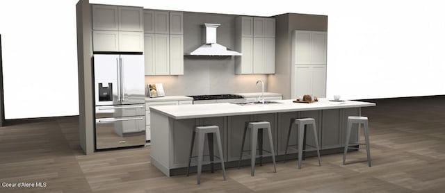 kitchen with wall chimney exhaust hood, stainless steel refrigerator with ice dispenser, light countertops, a center island with sink, and a breakfast bar area