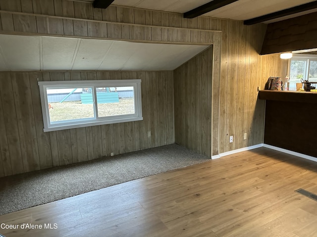 empty room featuring lofted ceiling with beams, wood finished floors, visible vents, and wood walls