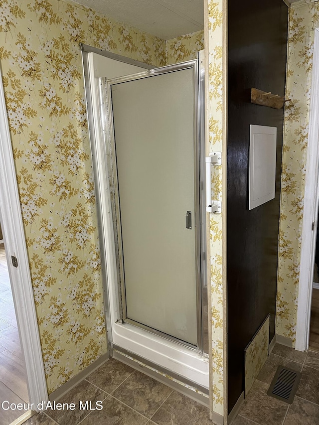 bathroom with wallpapered walls, a shower stall, and tile patterned floors