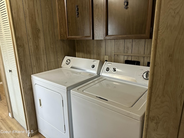 washroom featuring washing machine and clothes dryer, wooden walls, cabinet space, and light wood-style flooring