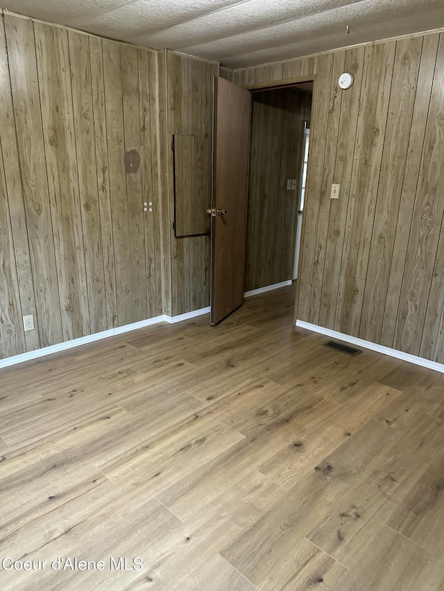 unfurnished room with hardwood / wood-style floors, baseboards, visible vents, and wood walls