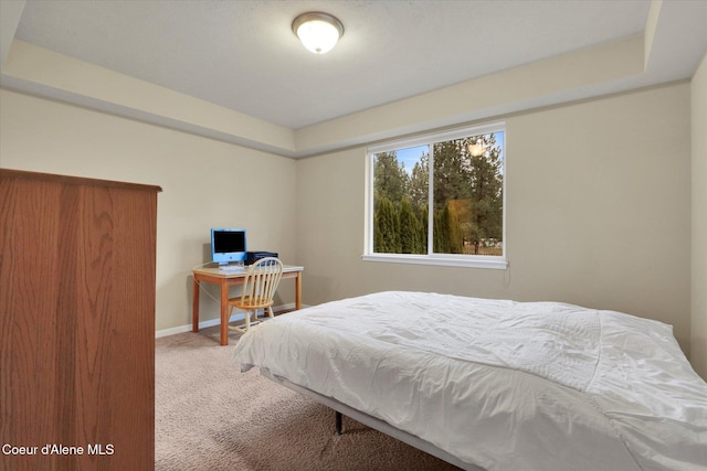 carpeted bedroom with baseboards and a raised ceiling