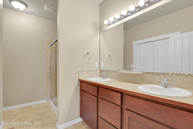 bathroom featuring a shower stall, double vanity, baseboards, and a sink