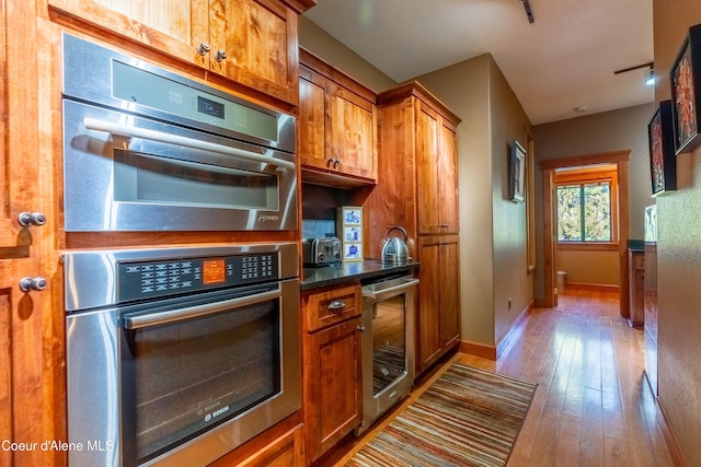 kitchen with baseboards, beverage cooler, hardwood / wood-style flooring, brown cabinetry, and stainless steel double oven