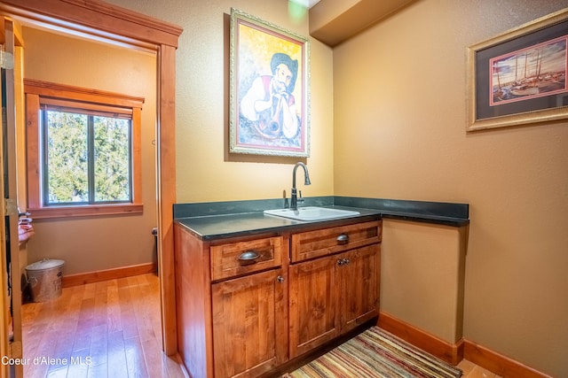 bar featuring wood finished floors, baseboards, and a sink