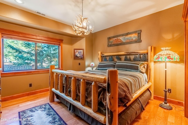 bedroom featuring visible vents, a notable chandelier, baseboards, and light wood-type flooring