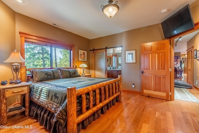 bedroom featuring light wood finished floors, visible vents, baseboards, a barn door, and ensuite bath