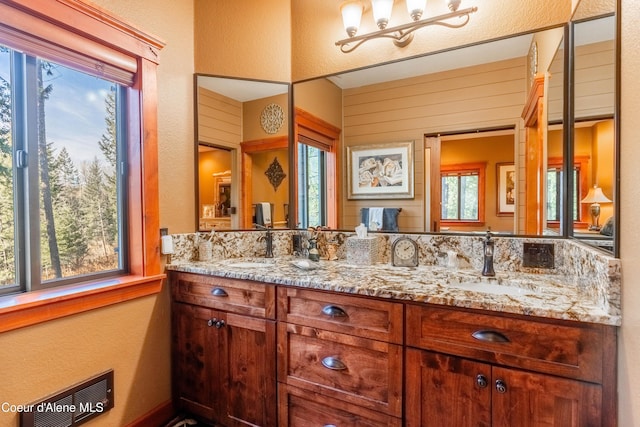 full bath with double vanity, visible vents, wood walls, and a sink