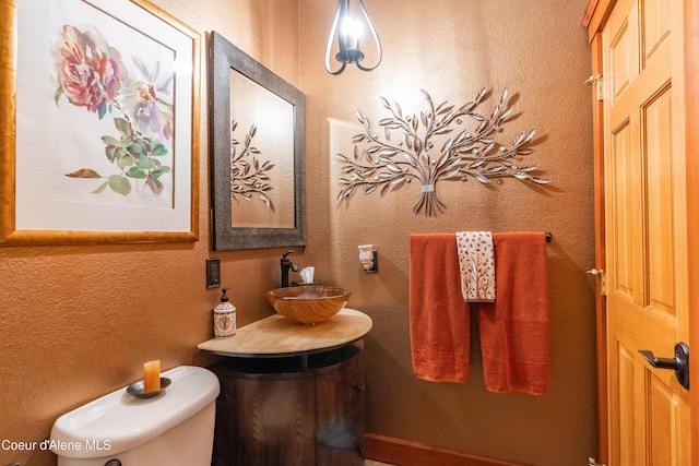 bathroom featuring toilet, a textured wall, and a sink