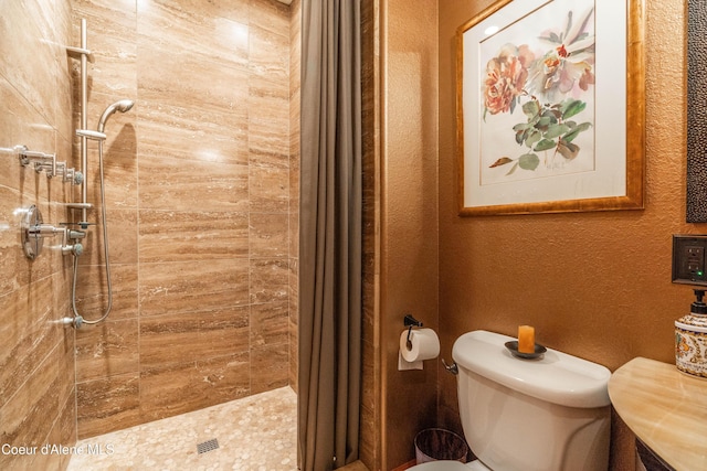 bathroom featuring toilet, a textured wall, and a tile shower