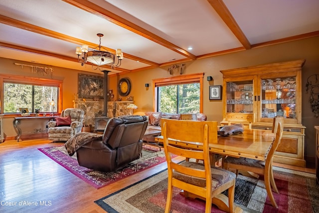 dining room featuring beam ceiling, a wood stove, an inviting chandelier, and wood finished floors