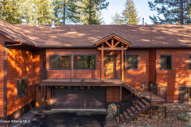 rustic home featuring stairway, a garage, and roof with shingles