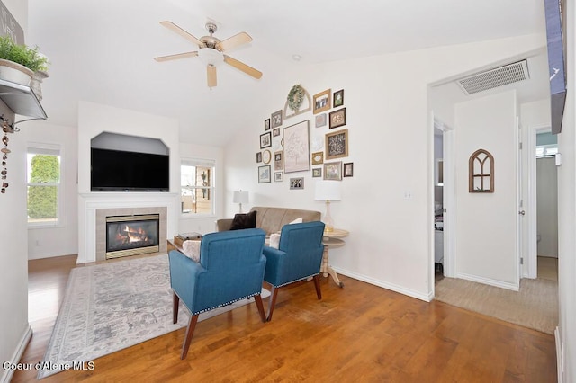 living area with visible vents, lofted ceiling, a tile fireplace, wood finished floors, and a ceiling fan