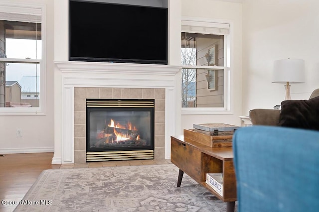 living room featuring a tile fireplace, baseboards, and wood finished floors