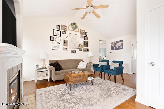 living room featuring a glass covered fireplace, vaulted ceiling, wood finished floors, and a ceiling fan