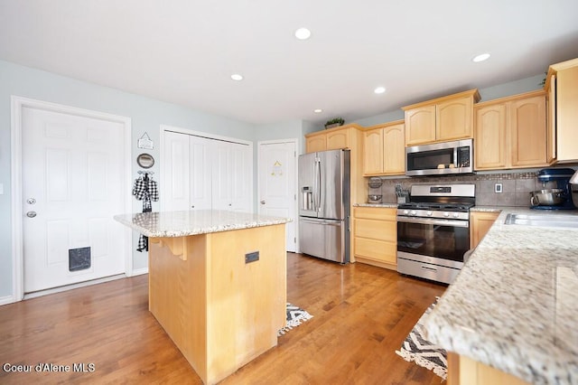 kitchen featuring tasteful backsplash, a center island, light brown cabinetry, appliances with stainless steel finishes, and a sink