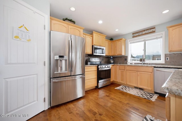 kitchen featuring tasteful backsplash, light brown cabinetry, wood finished floors, stainless steel appliances, and a sink