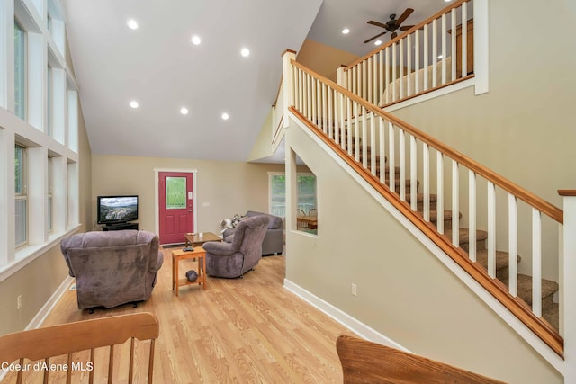 living room with stairway, light wood-style flooring, baseboards, and a towering ceiling