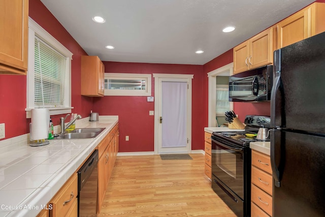 kitchen with tile counters, recessed lighting, light wood-style flooring, black appliances, and a sink