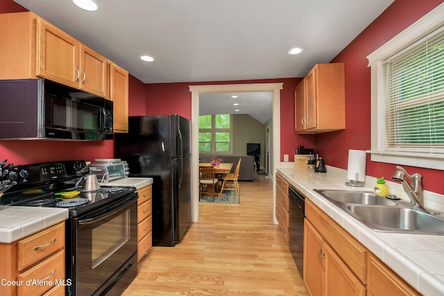 kitchen with black appliances, a sink, tile countertops, light wood-style floors, and lofted ceiling