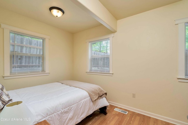 bedroom with beam ceiling, wood finished floors, visible vents, and baseboards